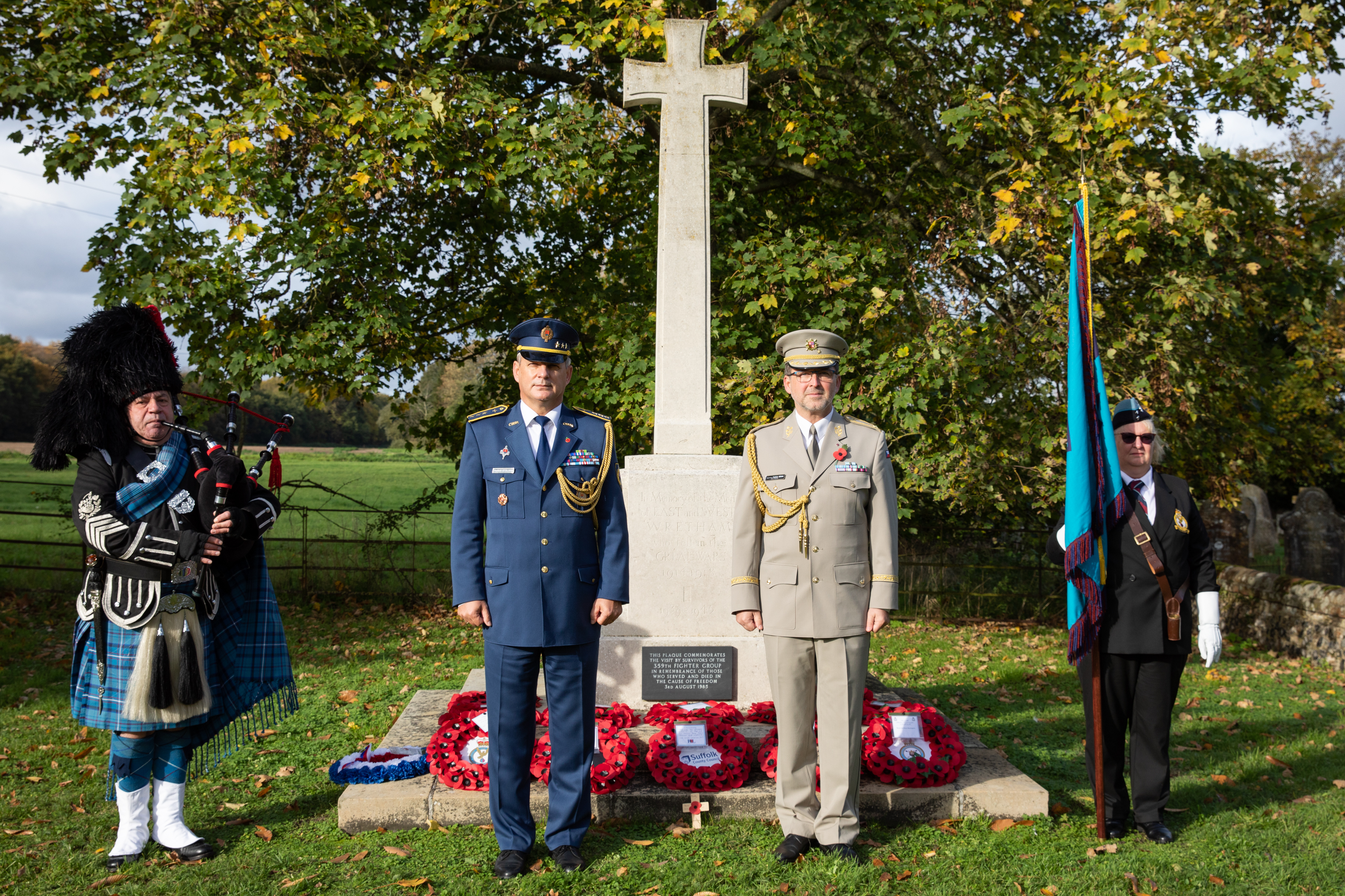 Image shows RAF aviators standing by memorial laid with poppy wreaths.